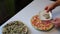 Preparation of pizza. The man sprinkles oregano pizza with crab sticks. Next to the table is a pizza, ready for cooking and other