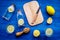 Prepare refreshing beverage lemonade. Lemons, juicer, bottle, knife, cutting board on blue wooden background top view