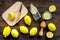 Prepare refreshing beverage lemonade. Lemons, juicer, bottle, knife, cutting board on dark wooden background top view