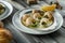 Prepared snails with butter sauce, white bread and spice on white salty plate on wooden background. Snails baked with