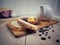 Preparing breakfast with slice of bread, yellow butter, blueberry fruit jam, white teapot on wooden cutting board.