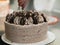 preparing brown frosted icing cup cake with cookies on top