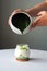 Preparing matcha latte green tea with milk in a glass on white table over gray background