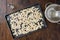 Preparing to roast fresh pumpkin seeds, baking sheet with washed seeds, bowl, saltshaker, on wood table