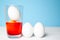 Prepearing for Easter. White eggs is coloring painting in glass with orange color. blue background. copyspace