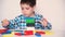 A preschool boy plays table jenga, carefully builds a tower of colorful wooden blocks