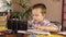 A preschool boy is talking with a teacher while looking at his smartphone and writes in a notebook.