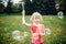 Preschool Caucasian blonde girl blowing soap bubbles in park on summer day. Child having fun outdoors. Authentic happy childhood