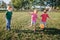 Preschool Caucasian girl and boys friends playing soccer football on playground grass field outside. Happy authentic candid