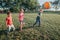 Preschool Caucasian girl and boys friends playing soccer football on playground grass field outside. Happy authentic candid