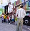 Preschool children standing in a line in front of a book bus and listening to a teacher tell a story about books