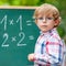 Preschool kid boy with glasses at blackboard practicing mathemat