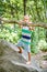 Preschooler boy climbs on rock against blurry green trees