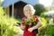 Preschooler boy holding seedling in plastic pots in the domestic garden on summer sunny day. Little farmer. Seasonal working in