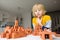 Preschooler boy is playing with real small clay bricks at the table at home. Child having fun and building smart constructions.