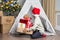 A preschooler boy in a Santa hat hides his gifts in a children& x27;s tent wigwam in the nursery. The child wants to be