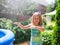 Preschooler cute girl playing with garden sprinkler. Summer outdoor water fun in the backyard.