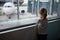 Preschooler girl in international airport, looking through the window at planes