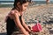 Preschooler girl playing with rake and pink toy bucket with sand, building sandy shapes and castles, enjoying sunbathing and