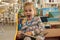 Preschooler little girl sitting and reading a book in library. Kid with books near a bookcase. Happy, cheerful and cute girl read