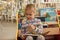 Preschooler little girl sitting and reading a book in library. Kid with books near a bookcase. Happy, cheerful and cute girl read