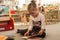 Preschooler little girl sitting and reading a book in library. Kid with books near a bookcase. Happy, cheerful and cute girl read