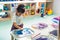 preschooler standing at the table and putting her hands in the watercolor, nursery medium shot