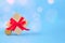 Present box with red bow and Christmas tree decorations on festive blue background with blurred bokeh and copyspace for your text