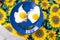 Present food plate - funny food faces smile fried eggs eyes vegetable mouth on blue dish yellow sunflowers cloth .