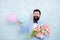 Present for spouse. Guy with air balloons. Birthday party. Bearded man hipster with flower bouquet. Womens day. Bearded