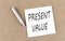 PRESENT VALUE text on a sticky note on cork board with pencil