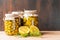 Preserved fermented olives and artichokes in oil in glass jars with wild fennel and lemon cut on dark wooden background.