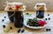 Preserved homemade black currant jam in glass jars on light wooden table. Fresh berries and green leaves, white vintage plate