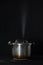 Pressure cooker releasing steam through the lid, against a black background