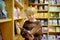 A preteen boy leafing through a book while standing at a bookshelf in a school library or bookstore