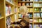 A preteen boy leafing through a book while standing at a bookshelf in a school library or bookstore