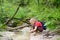 Preteen boy in red shirt is exploring nature and playing with water in brook during hiking in mountains valley. Active leisure for