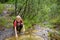 Preteen boy in red shirt is exploring nature and playing with water in brook during hiking in mountains valley. Active leisure for