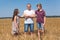 Preteen son and daughter looking at their single father, kids lay hands on his shoulders, wheat field