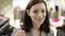 Pretty adult woman is looking to the camera, smiling and touching her hair at clothing store, close up face shot