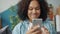 Pretty Afro-American lady using smartphone texting smiling indoors at home