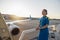 Pretty air stewardess in blue uniform smiling away, standing outdoors at the sunset. Commercial airplane near the