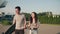 Pretty asian girl and handsome guy during orange sunset passing by architectural building or park with a board and