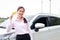 Pretty Asian girl standing next to the car smiling happily.