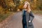 Pretty attractive young woman in a stylish gray coat in a green trendy blouse in vintage jeans walks in a park with golden foliage