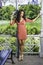 A pretty black woman with long curly hair is standing by a pavilion in a park, charmingly looking at you