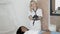 Pretty blond female doctor cosmetologist preparing for beauty procedures, wearing black latex gloves. Her patient, young