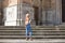 Pretty blonde adult woman dressed in jeans and white top having fun posing for photos on the steps of the cathedral in Cadiz,