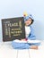 Pretty blonde girl with cozy blue unicorn costume with blackboard with different words on it like love and peace and some more