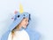 Pretty blonde girl with cozy blue unicorn costume is posing in the studio in front of blue wall and is happy